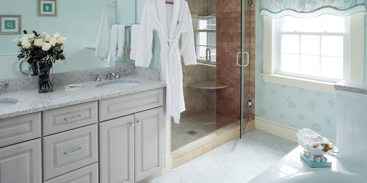 A bright, elegant bathroom with a double vanity and a glass shower. A white robe hangs on the shower door, ready for use.