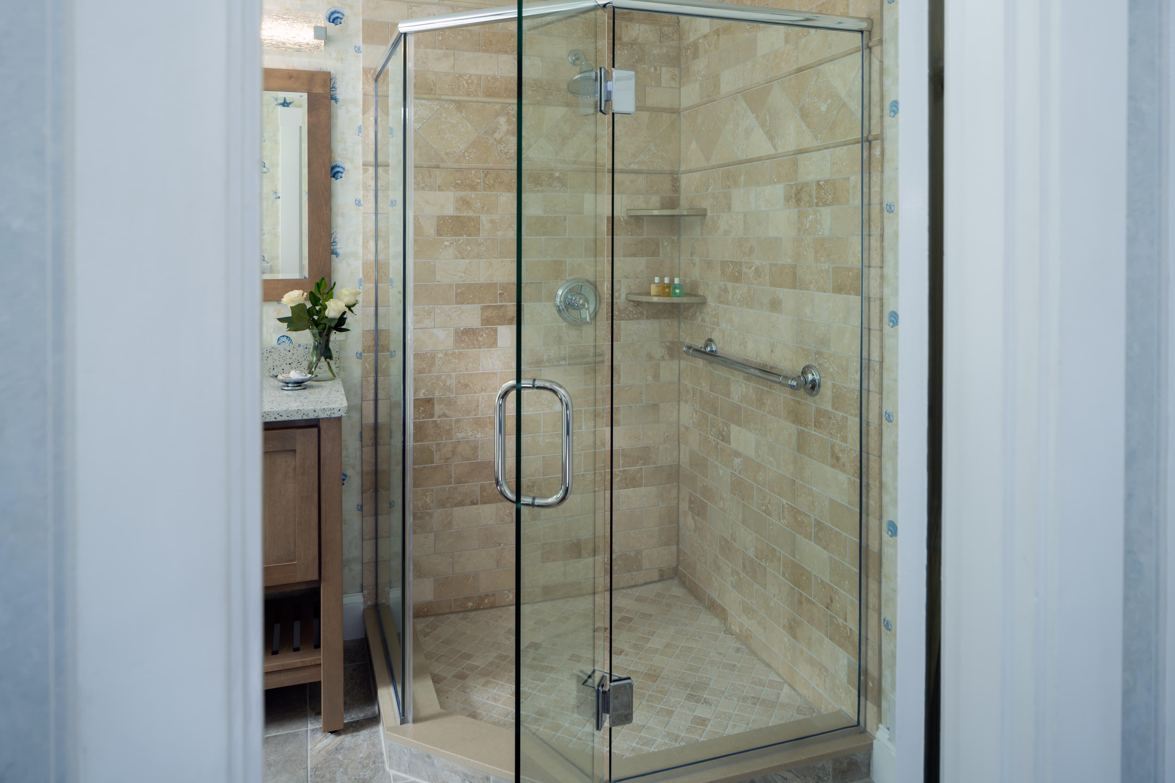 A bright bathroom with a frameless glass shower enclosure. The shower walls and floor are tiled , with a metal grab bar on the wall.