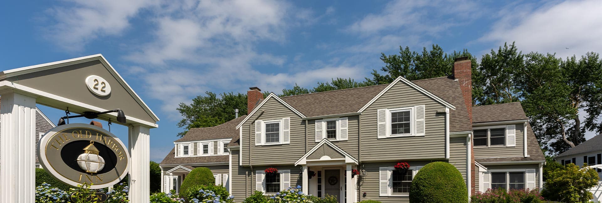 A charming two-story inn with a sign reading "The Old Harbor Inn" in front, set against a clear blue sky.
