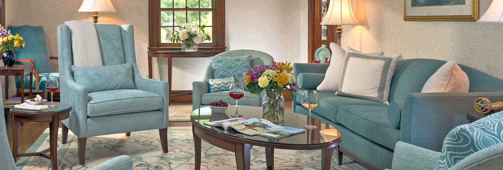 A cozy, softly lit living room featuring light blue furniture, a floral centerpiece, and a coffee table with snacks and drinks.