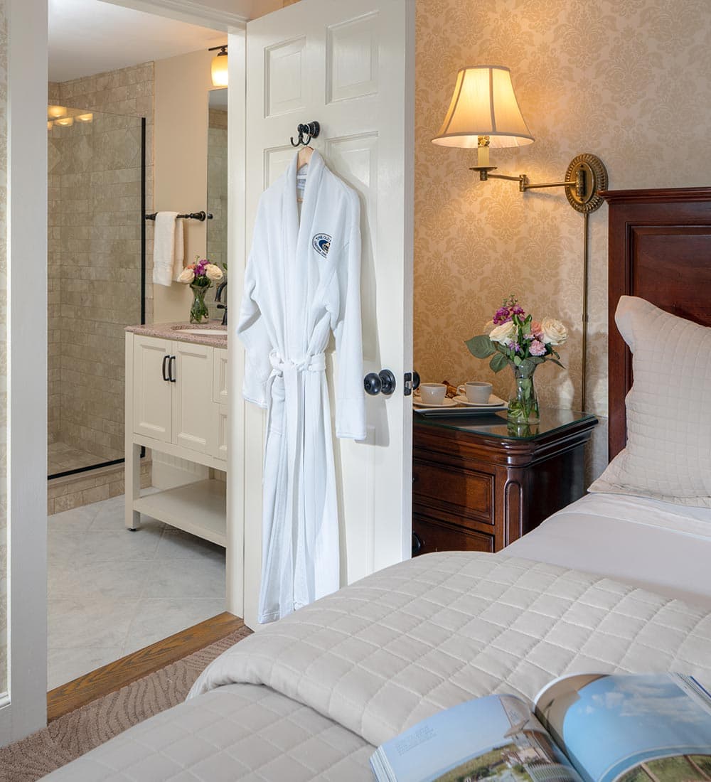 A cozy hotel room featuring a robe hanging on the door, with a bathroom visible in the background.