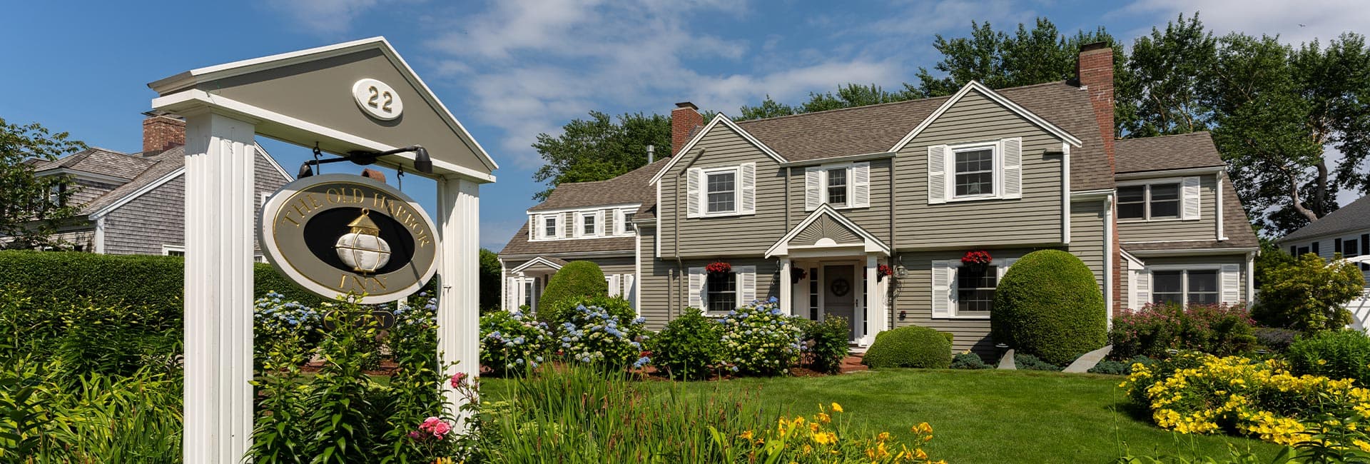 A charming two-story house with a well-kept garden and a sign reading "The Old Harbor Inn" at the entrance.