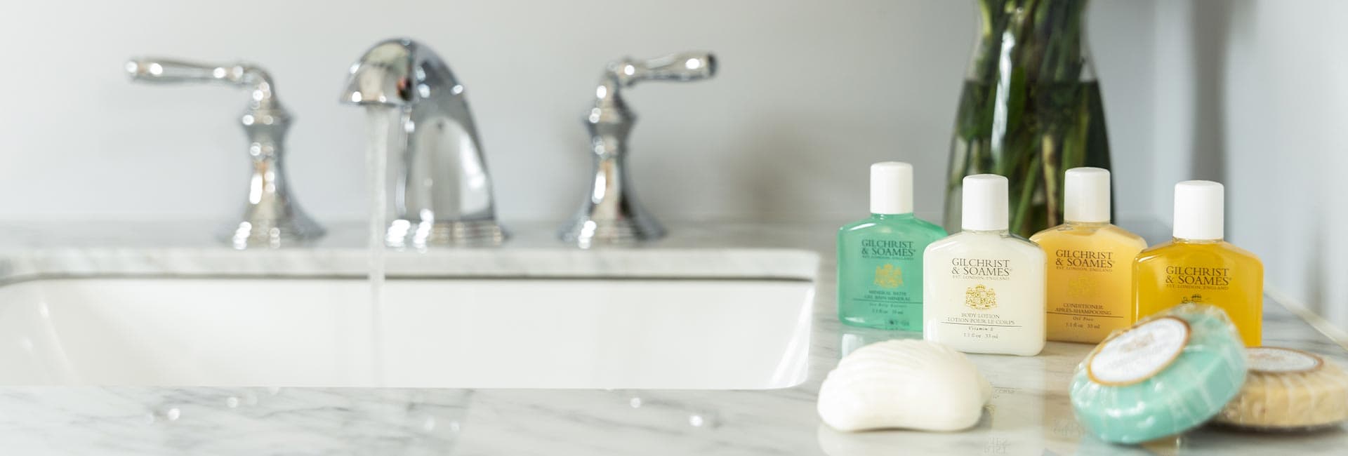 A marble countertop featuring various bottles of bath products and a shell-shaped soap with a faucet in the background.