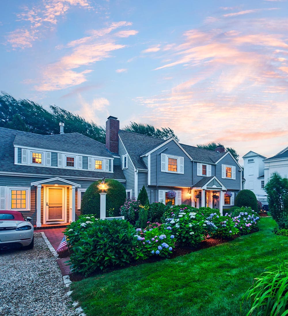 A charming house with landscaped gardens and a driveway at dusk, under a colorful sky.