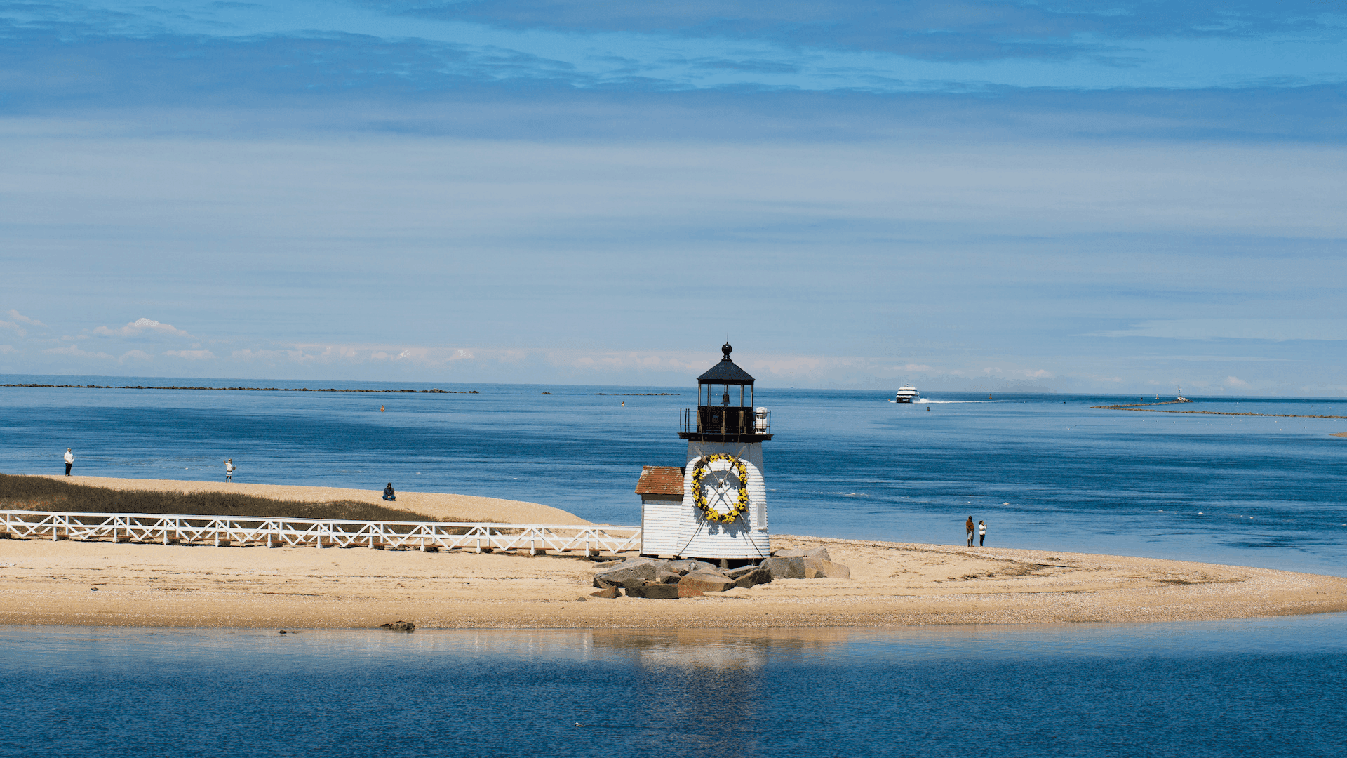 A lighthouse stands on a sandy shoreline beside a calm blue sea under a clear sky. A lighthouse stands on a sandy shoreline beside a calm blue sea under a clear sky.