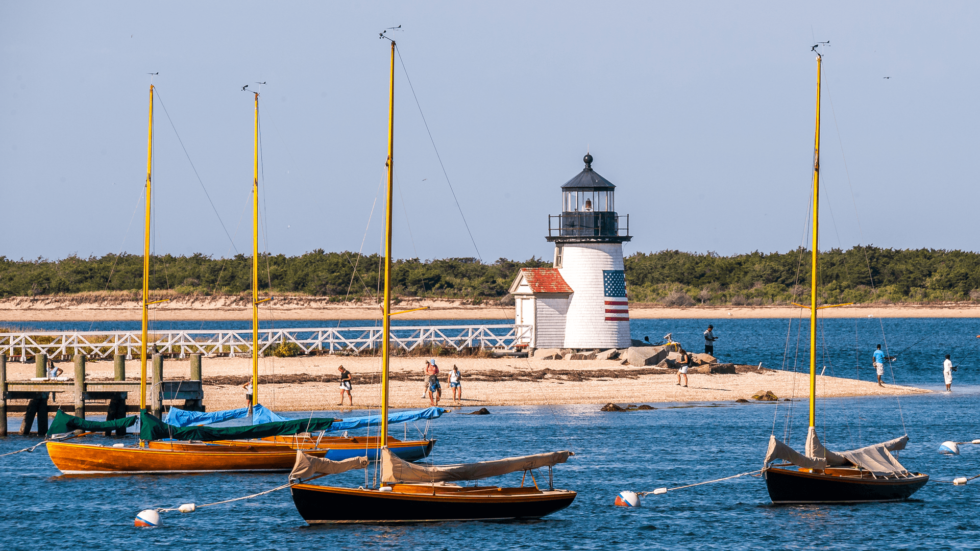 A lighthouse stands near a sandy beach, with sailboats floating in the foreground. A lighthouse stands near a sandy beach, with sailboats floating in the foreground.
